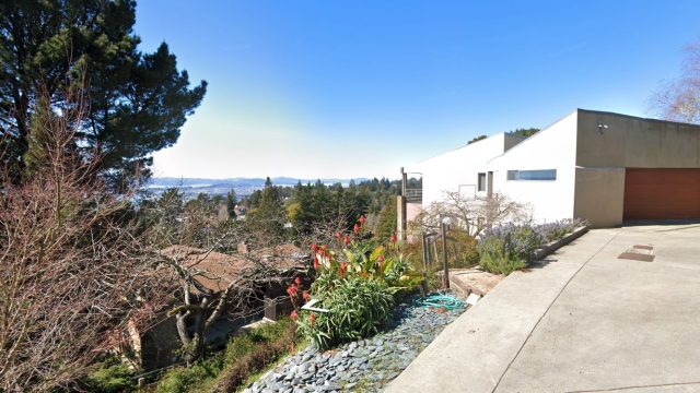 Street view of 37 Hill Road. Modern white house with garage on hillside overlooking valley