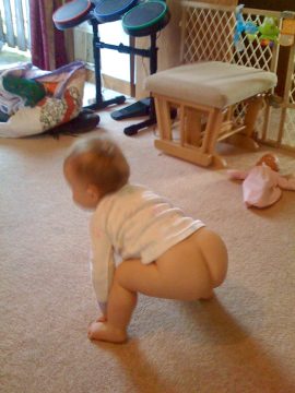 A baby crawling on a carpeted floor in a room with toys and furniture.