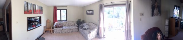 A living room with two floral sofas, a sliding glass door, wall art, and a person sitting in a chair.