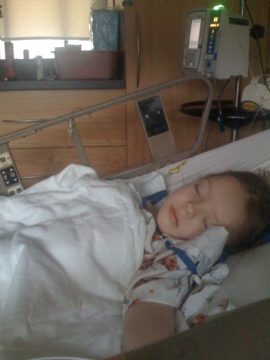 A young child sleeping in a hospital bed with medical equipment nearby.