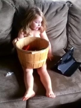 A young child sitting on a couch holding a large wooden basket with items inside.