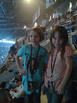 Two young children wearing lanyards with ID cards stand in stadium seating.