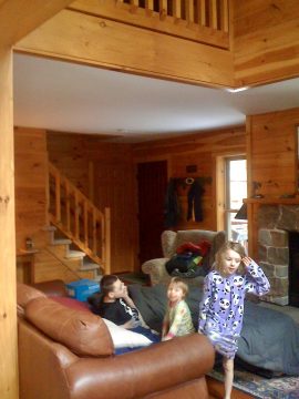 Three children in pajamas sitting on a couch in a wooden cabin living room.