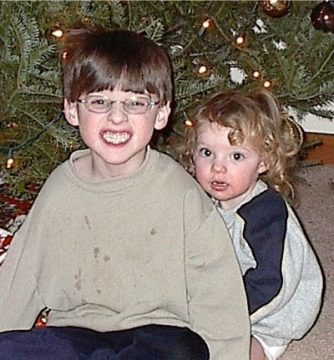 Two young children sitting in front of a decorated Christmas tree.