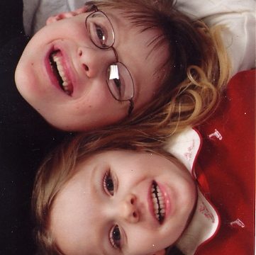 Two smiling children with glasses lying on their backs together.