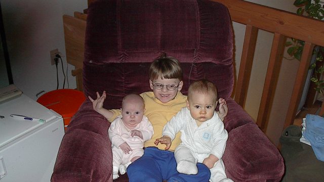 Three young children sitting together in a large purple armchair.
