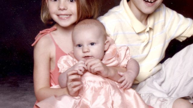 Three young children sitting together in a studio photo; two older kids flanking a baby.