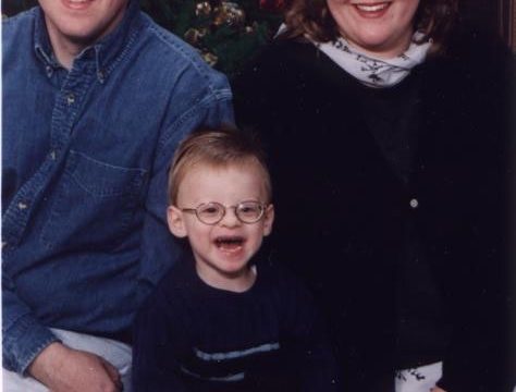 A family portrait featuring a man, woman, and young child sitting together in front of a Christmas tree.