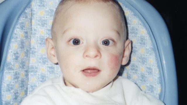 A young child with light hair sitting in a blue high chair looking forward.