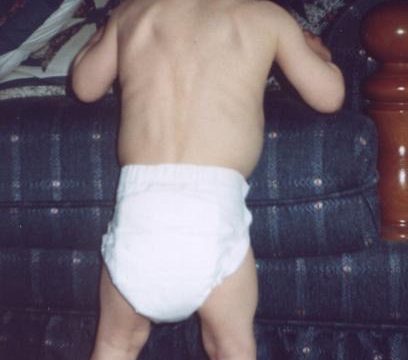 A toddler in a diaper standing with back to camera on blue couch