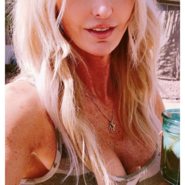 A woman with long blonde hair wearing a camouflage tank top, holding a green glass jar, displayed on the Bumble app interface.