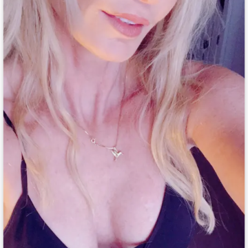 A woman with blonde hair wearing a black top and necklace in a dating app profile view
