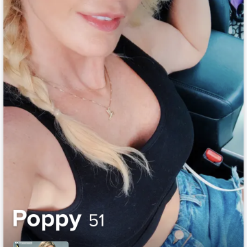 A woman with blonde hair in a braid wearing sunglasses and a black top, sitting inside a vehicle with music playing.