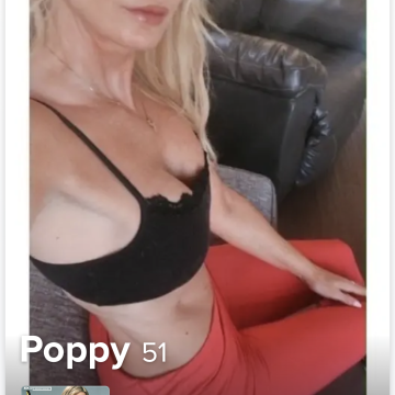 A woman with blonde hair wearing a black top and red pants sitting on a couch in a living room setting.